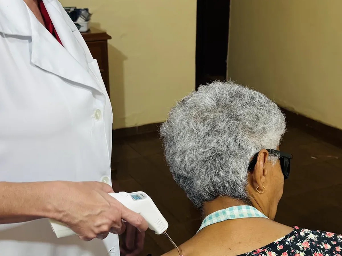 Taisa aplicando laser no ombro de uma paciente idosa